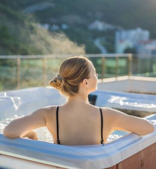 Eine Frau sitzt entspannt in einem Whirlpool, Die Sonne scheint und sie ist umgeben von Natur