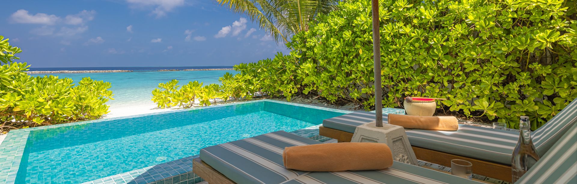 Zwei Liegen unter einem Sonnenschirm, vor einem kleinen Pool