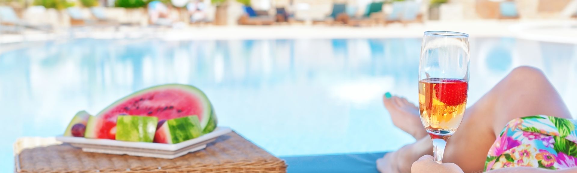 Person liegt am Pool mit Obst und Getränk