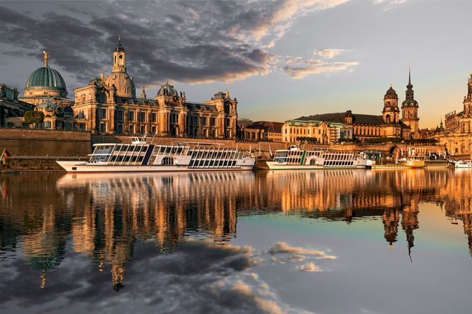 Flusskreuzfahrschiffe fahren an alten Bauwerken vorbei, die sich im stillen Wasser des Flusses spiegeln