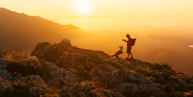 Mann und Hund wandern zusammen in den Bergen bei Sonnenuntergang