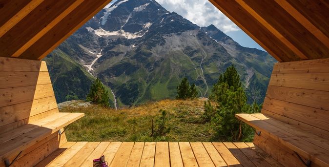 Aus einer Holzhütte mit zwei Bänken schaut man auf eine beeindruckende Berglandschaft