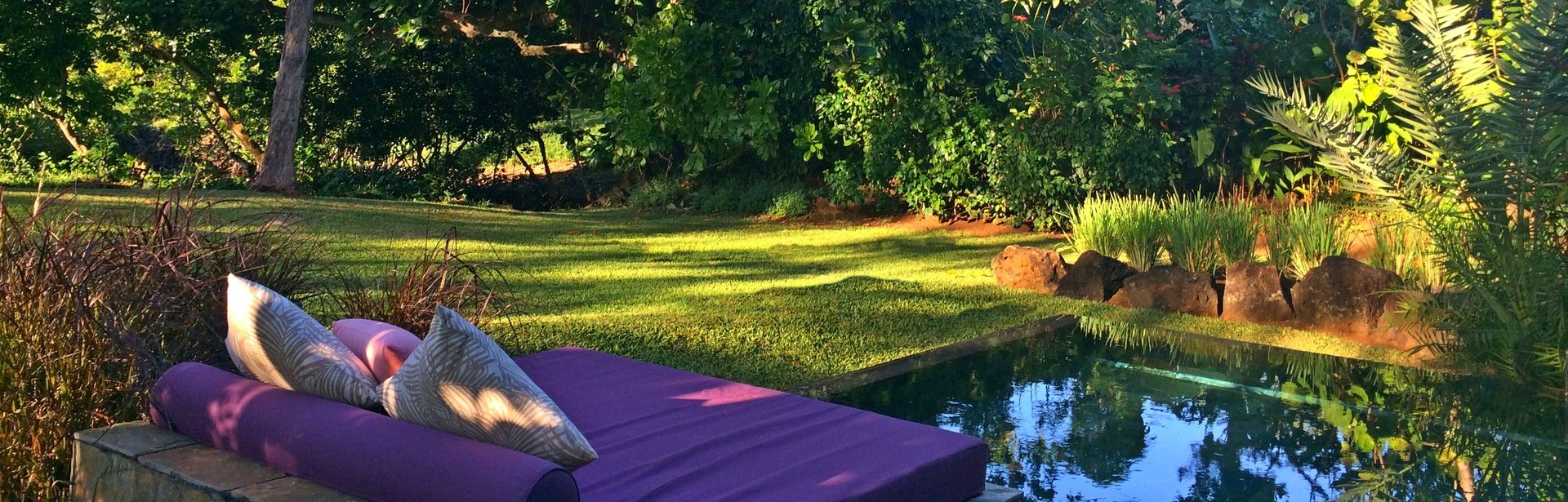 Im Schatten von Bäumen steht in einem Garten eine Lila Liege an einem kleinen Teich