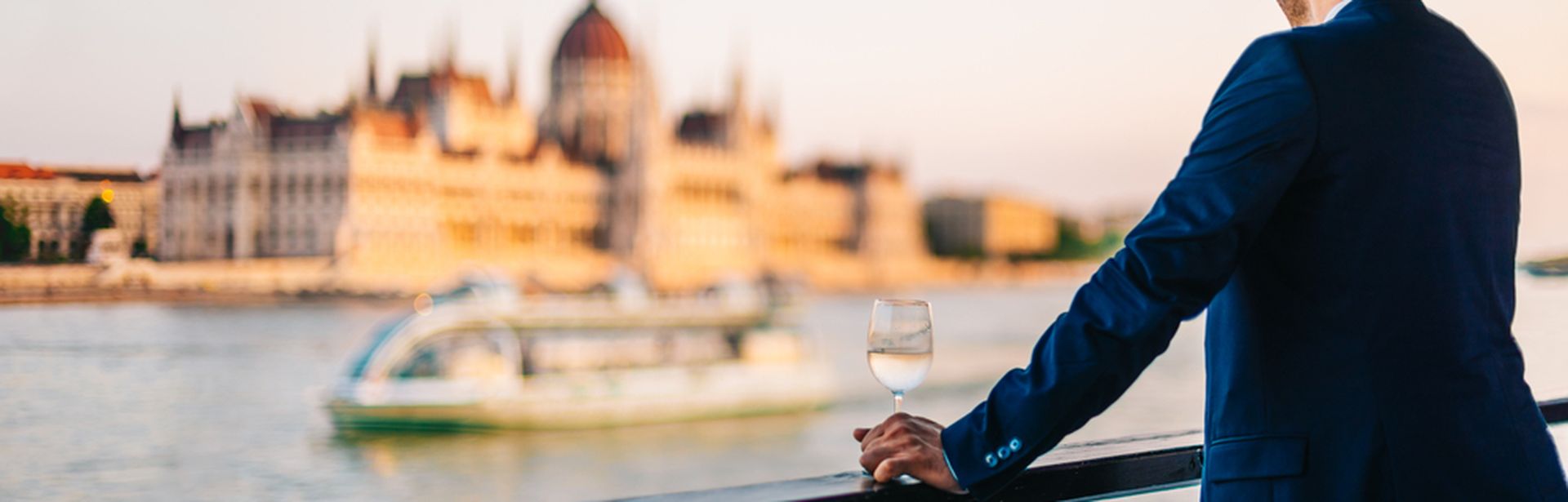 Mann steht an der Reling eines Kreuzfahrtschiffes und schaut sich die vorbeiziehenden Gebäude am Ufer an