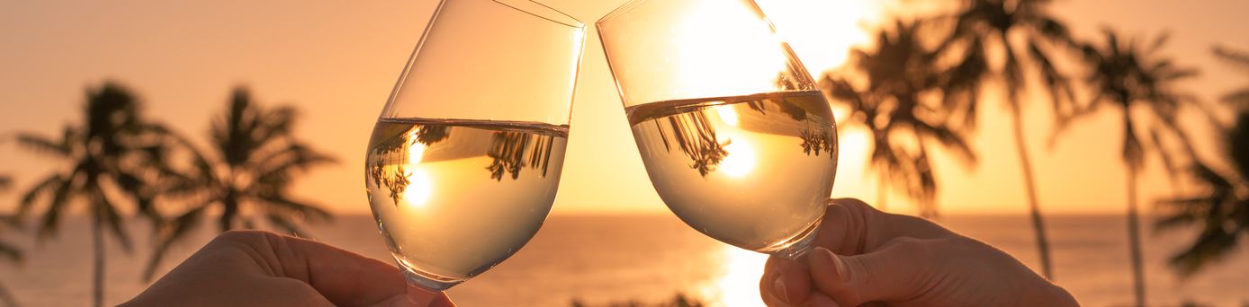 Zwei Hände stoßen am Strand mit Weingläsern an 