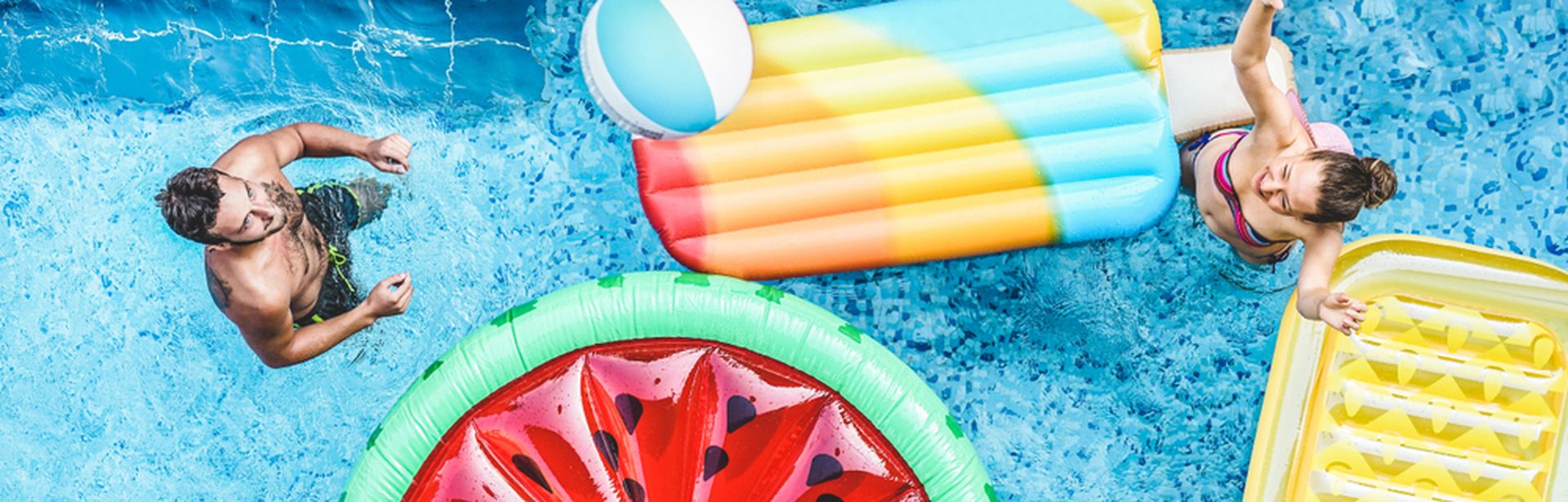 Ein Pool von oben, mehrere Personen und Pool Floaties in Frucht Formen
