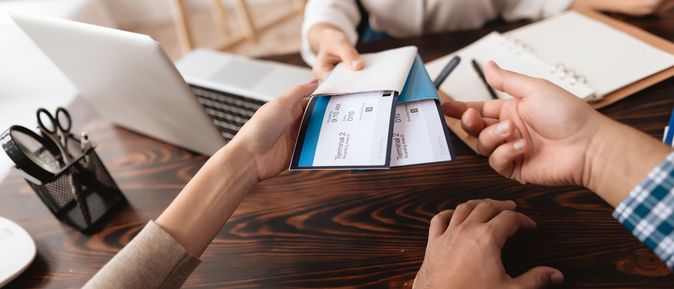 Eine Frau sitzt am Schreibtisch und übergibt zwei Personen Ihre Flugtickets