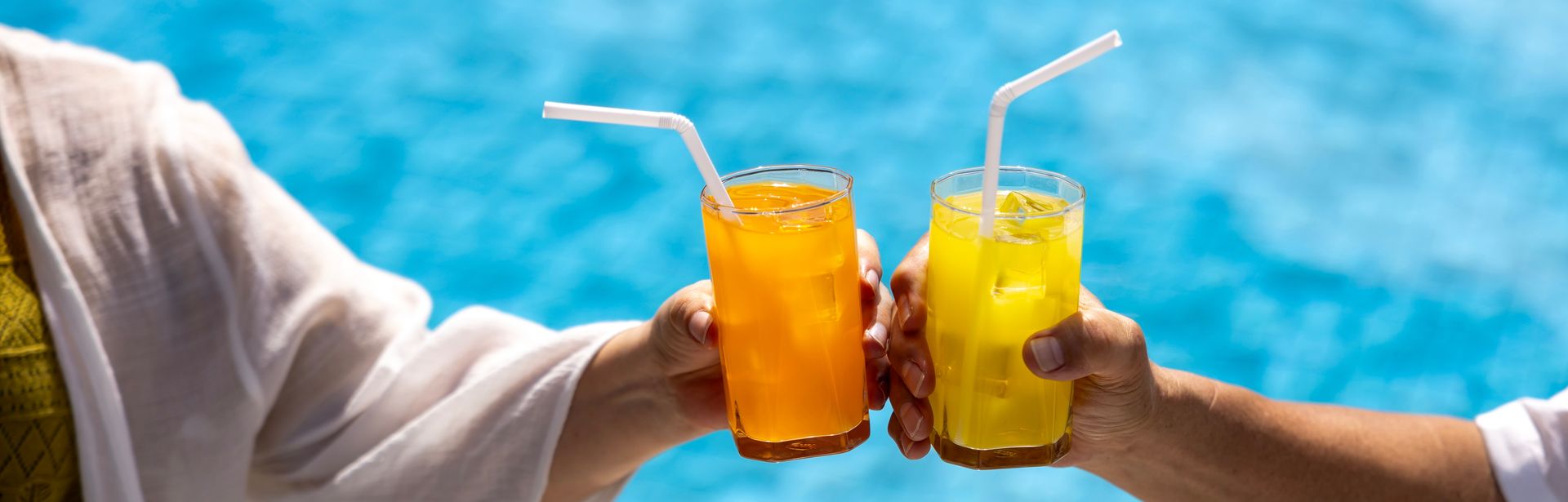 Zwei Hände stoßen mit Gläsern über einem Pool an