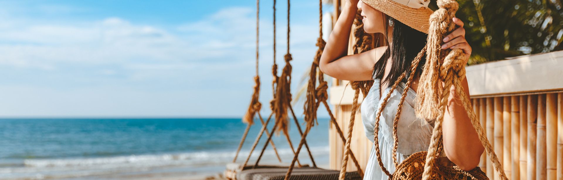 Eine Frau sitzt am Strand auf einer Schaukel und schaut in die Ferne in Richtung Meer