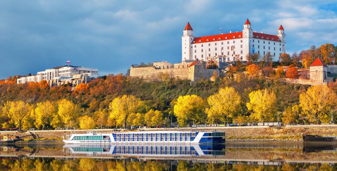 Flusskreuzfahrtschiff fährt an einer herbstlichen Landschaft mit einem weißen Schloss vorbei