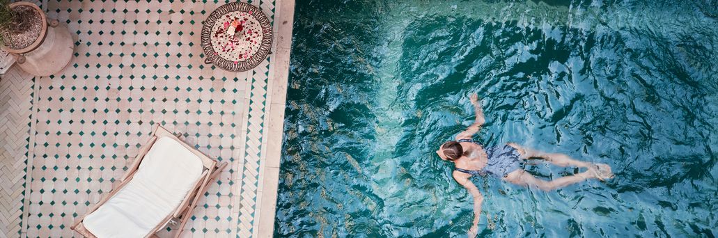 Frau schwimmt in einem Pool; Neben dem Pool, auf der Terrasse steht eine Liege