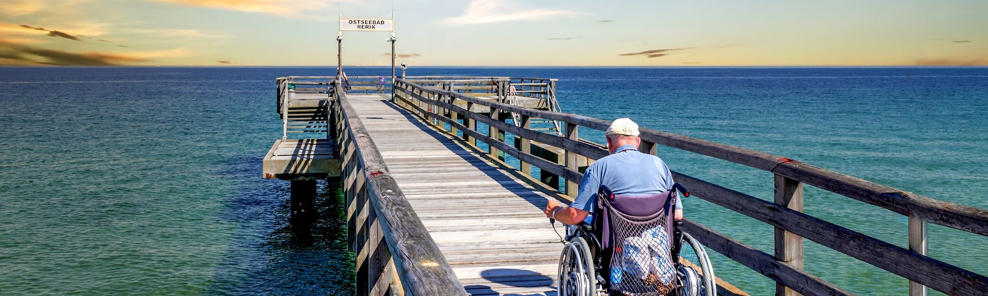 Mann im Rollstuhl auf einer Seebrücke am Meer