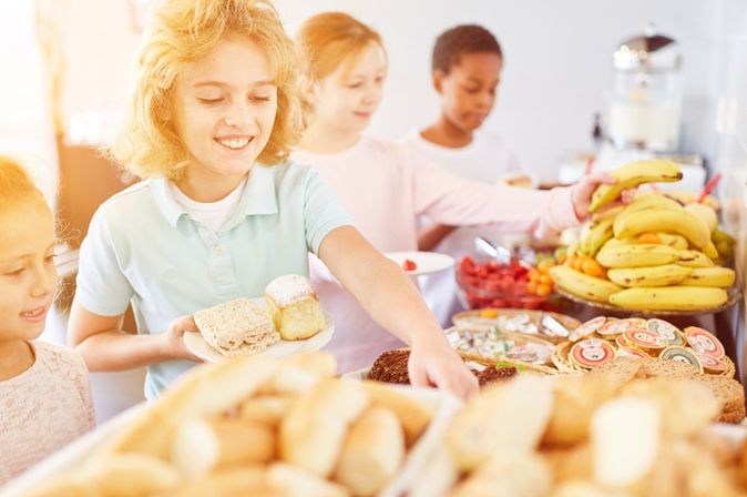 Vier Kinder bedienen sich lächelnd an einem Frühstücksbuffet