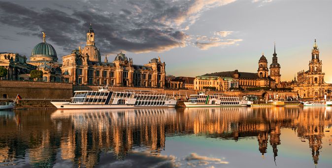 Flusskreuzfahrschiffe fahren an alten Bauwerken vorbei, die sich im stillen Wasser des Flusses spiegeln