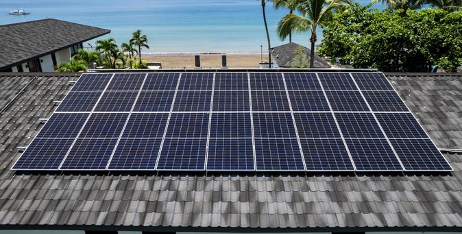 Ein Dach mit Solarplatten, im Hintergrund ein Strand und das Meer