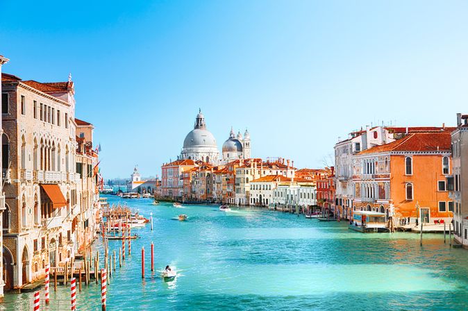 Blick auf den Canal Grande in Venedig, Italien. Links und rechts stehen historische Gebäude. Auf dem türkisblauen Wasser fahren kleine Boote.