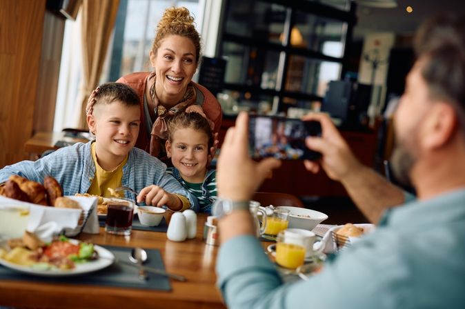 Ein Vater fotografiert seine Frau und Kinder am Frühstückstisch