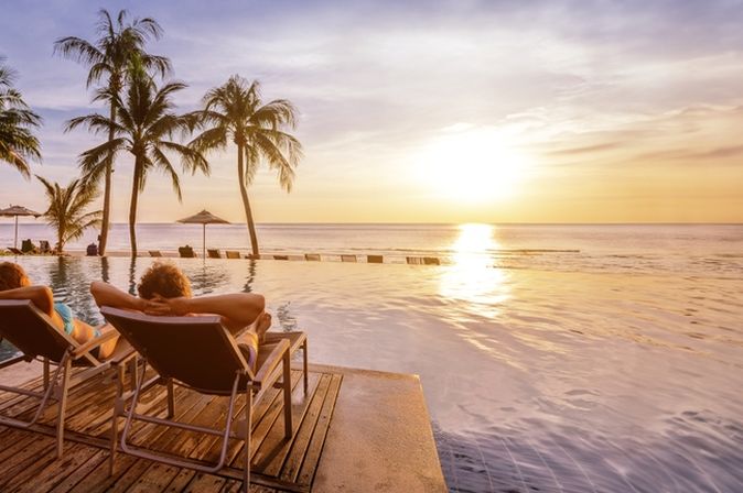 Zwei Personen liegen auf Liegen am Pool und schauen sich den Sonnenuntergang an