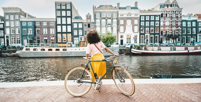 Frau mit Fahrrad schaut auf Häuser in Amsterdam
