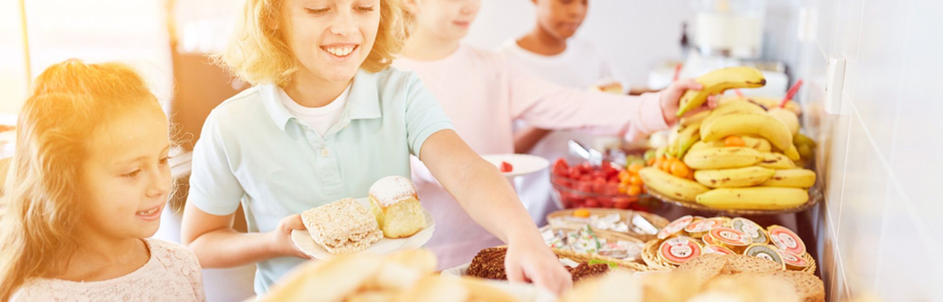 Vier Kinder bedienen sich lächelnd an einem Frühstücksbuffet