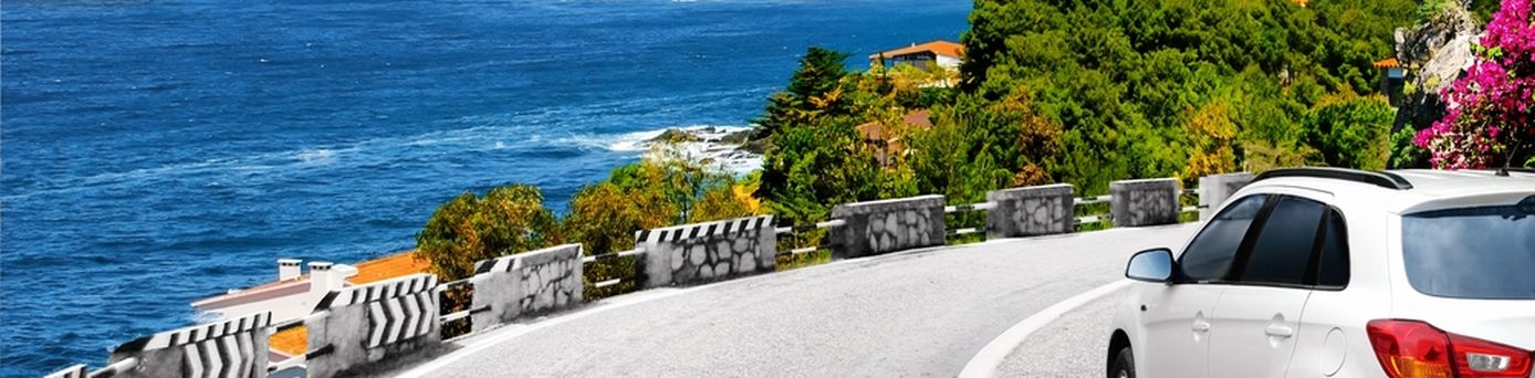 Ein weißes Auto fährt eine scharfe Kurve am Meer entlang