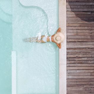 Eine Frau mit weißem Sonnenhut lehnt am Rand eines eleganten Pools