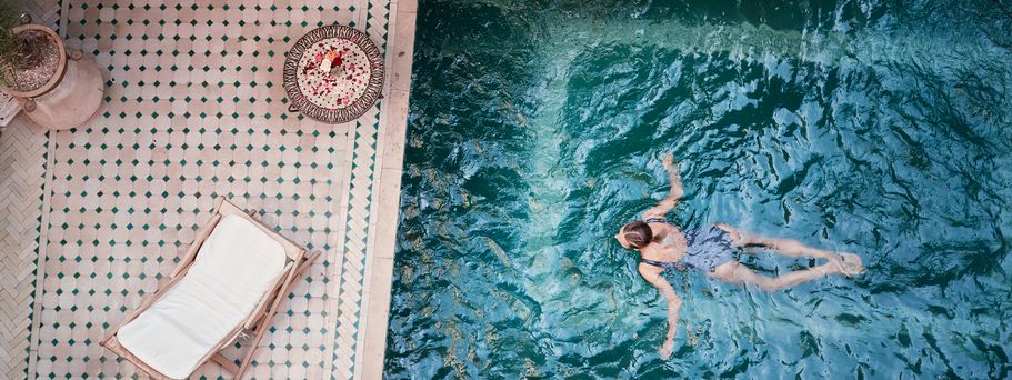 Frau schwimmt in einem Pool; Neben dem Pool, auf der Terrasse steht eine Liege