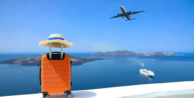 Ein Koffer steht auf einer Mauer, im Hintergrund sieht man das Meer und ein Schiff, im Himmel fliegt ein Flugzeug