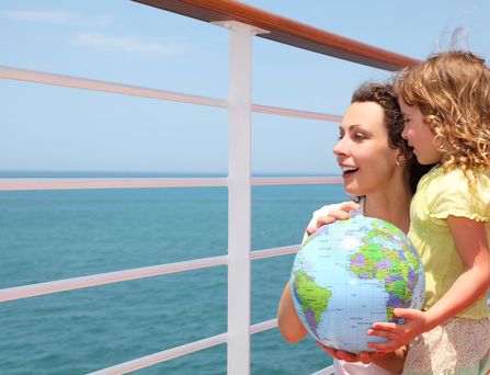 Mutter und Kind schauen über das Geländer eines Kreuzfahrtschiffes und halten einen Globus