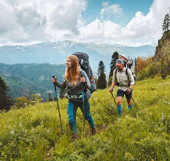 Zwei Personen wandern mit Nordic Walking Stöckern durch eine Wiese
