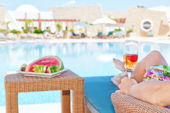 Person liegt am Pool mit Obst und Getränk