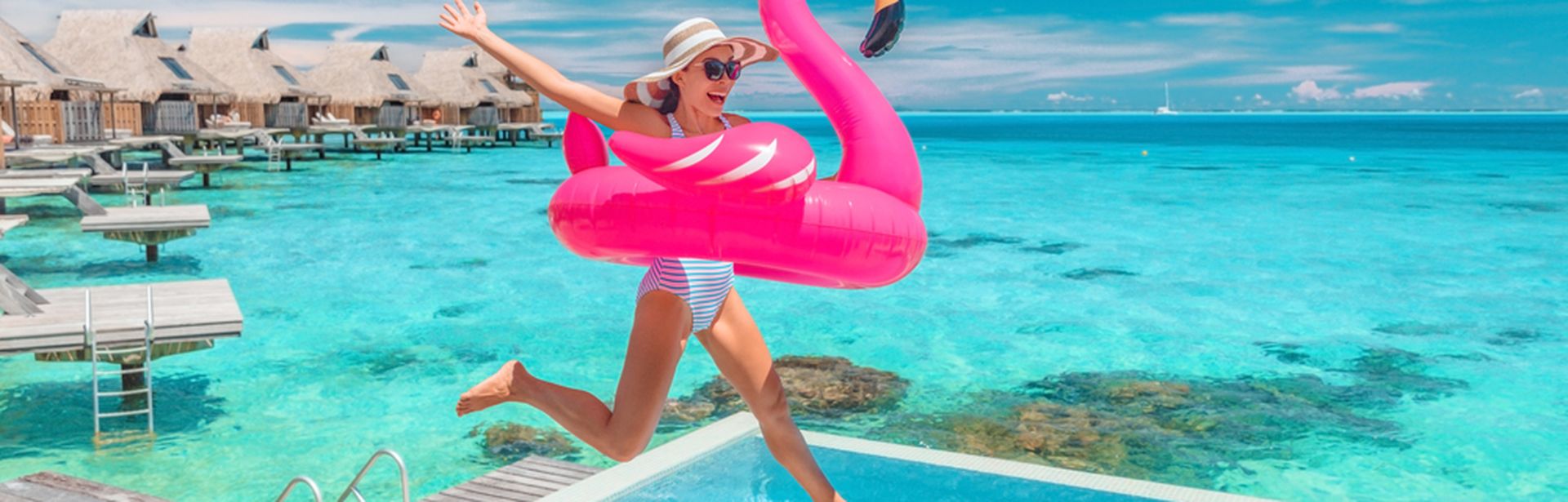 Eine Frau springt lachend mit einem Flamingo Schwimmreifen in einen Pool 