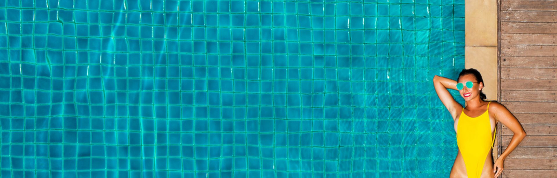 Ein großer Pool, am Rand liegt eine Frau im gelben Badeanzug und einer Sonnenbrille