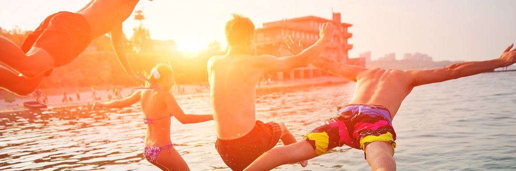 Vier Personen springen bei Sonnenuntergang ins Meer