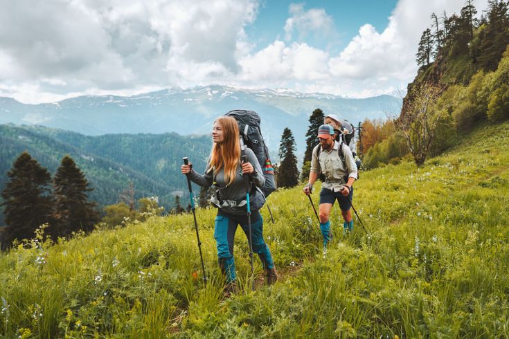 Zwei Personen wandern mit Nordic Walking Stöckern durch eine Wiese