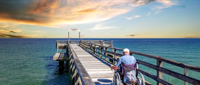 Mann im Rollstuhl auf einer Seebrücke am Meer