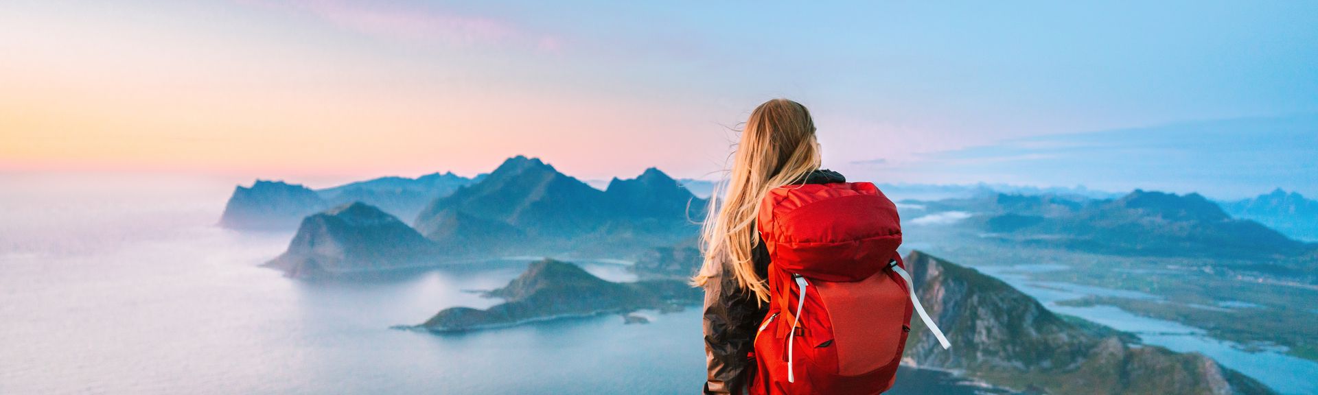 Eine Frau von hinten, Sie trägt einen großen Rucksack und schaut von einem Berg aus den Sonnenaufgang an