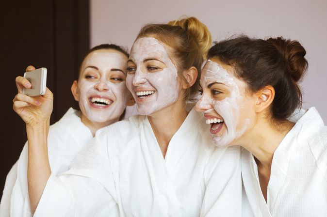 Drei Frauen tragen Gesichtsmasken und machen lachend ein Selfie
