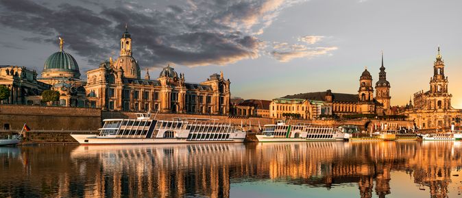 Flusskreuzfahrschiffe fahren an alten Bauwerken vorbei, die sich im stillen Wasser des Flusses spiegeln
