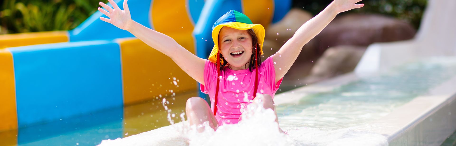 Ein glücklich aussehendes Kind rutscht durch eine Wasserrutsche und hebt die Arme