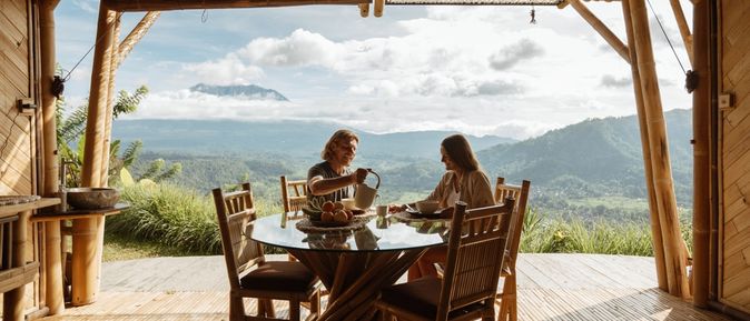Auf einer Terrasse mit beeindruckendem Ausblick auf eine grüne Landschaft sitzen zwei Personen an einem Tisch 