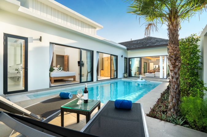 Ein Pool vor einer eleganten Villa mit zwei Liegen und einem Tisch