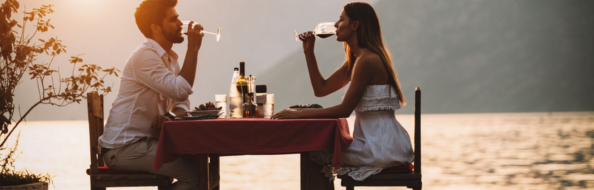 Eine Frau und ein Mann sitzen an einem Tisch am Wasser und trinken Wein