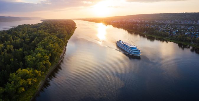 Flusskreuzfahrtschiff, dass bei Sonnenuntergang auf einem Fluss fährt
