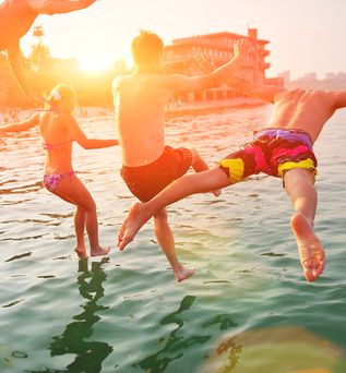 Vier Personen springen bei Sonnenuntergang ins Meer
