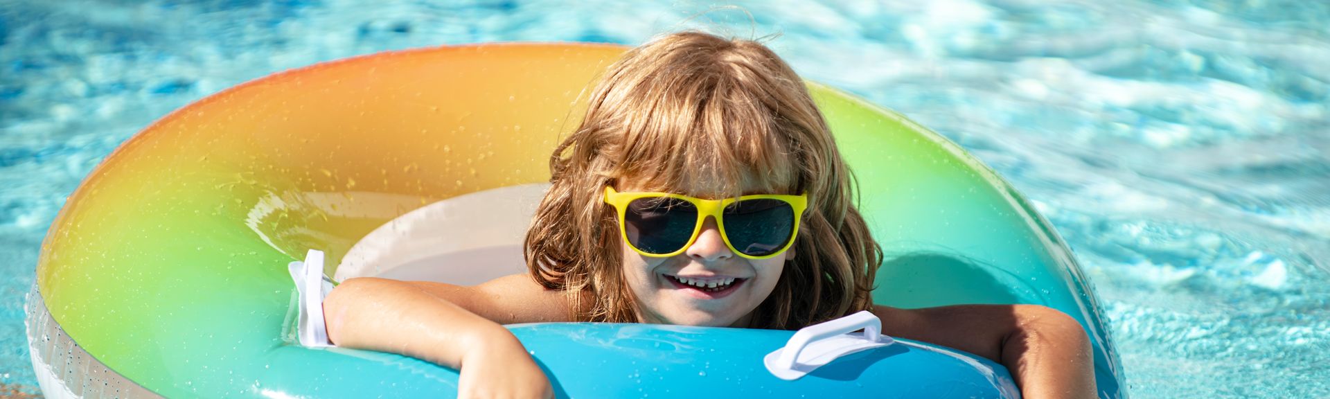 Ein Kind mit einer Sonnenbrille in einem bunten Poolring