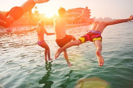 Vier Personen springen bei Sonnenuntergang ins Meer