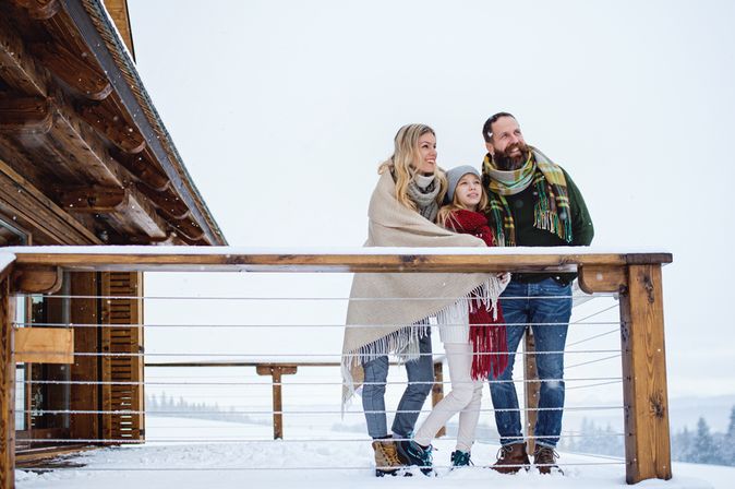 Familie steht in Winterklamotten auf der Terrasse eines Balkons während Schnee liegt