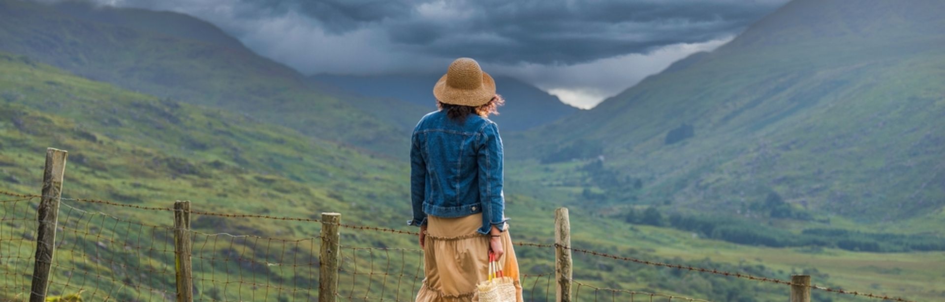 Frau steht auf einem Stein und blickt auf auf eine grüne Berglandschaft