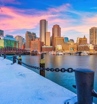 Schneebedeckter Weg am Hafen vor einem Fluss. Auf der anderen Flussseite sind Hochhäuser zu sehen